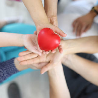 Red plastic heart close up. Many hand of women, men and children, one above one, hold heart.